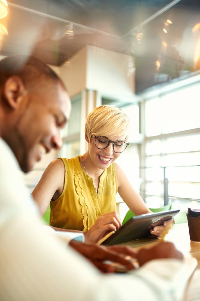 Two creative millenial small business owners working on social media strategy using a digital tablet while sitting at desk-1